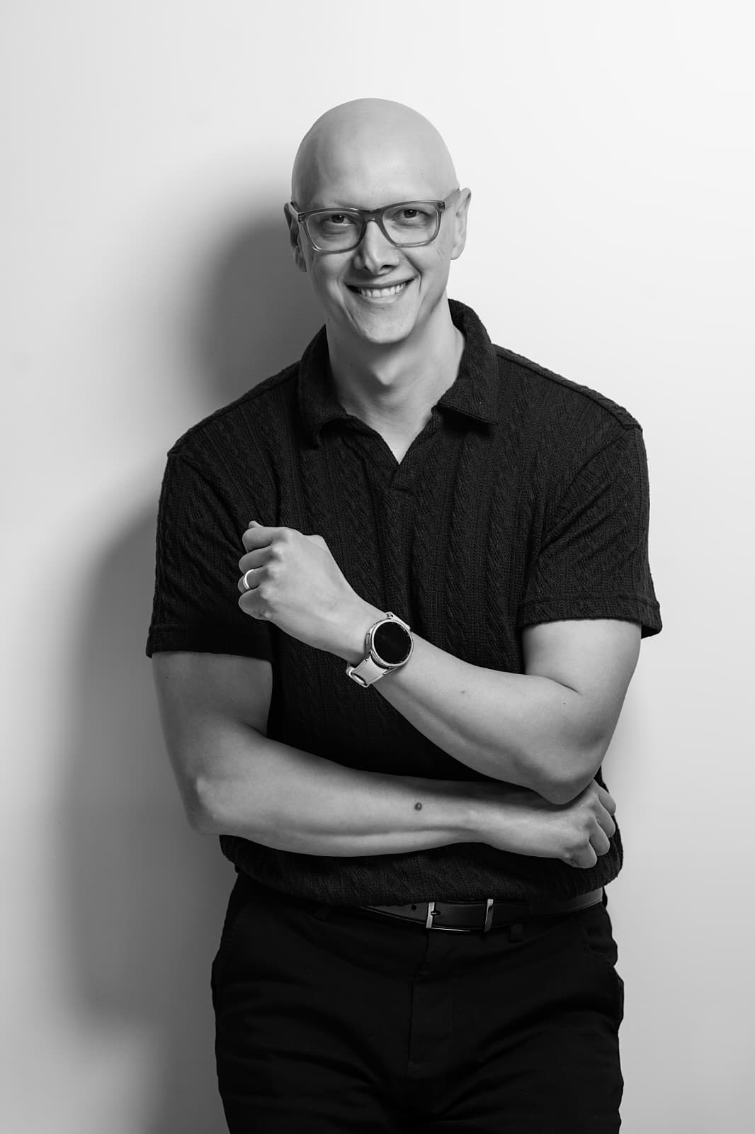 Black-and-white portrait of Moe Mojahed smiling, wearing glasses and a dark polo, arms folded